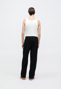 Λευκή αμάνικη μπλούζα και μαύρο παντελόνι φόρμας, με ελαστική μέση και πίσω τσέπη, συνδυασμένα με καφέ παπούτσια.