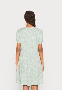 Grünes kurzärmliges Kleid mit floralem Muster, geraffter Taille und ausgestellt Rock. Der Stoff wirkt leicht und strukturiert.