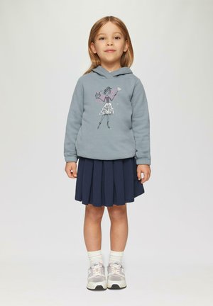 Hellblaues Kapuzenshirt mit grafischem Design. Kombiniert mit einem marineblauen Faltenrock und grauen Sportschuhen mit rosa Akzenten.