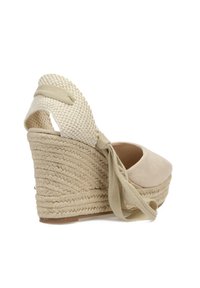 Zapato de cuña de esparto de ante beige con una correa de tela tejida y lazo de cinta. Presenta un tacón de cuña envuelto en yute con un acabado texturizado.