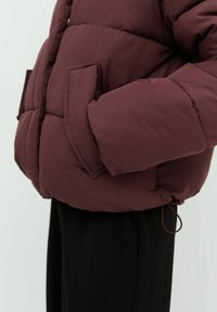 Giubbotto imbottito borgogna con ampie tasche laterali, motivo trapuntato e orlo elastico. Texture morbida con un leggero luccichio.