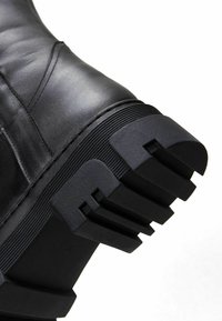 Stivaletto in pelle nera con tomaia texture, suola in gomma spessa con scanalature distintive e design con punta rotonda.