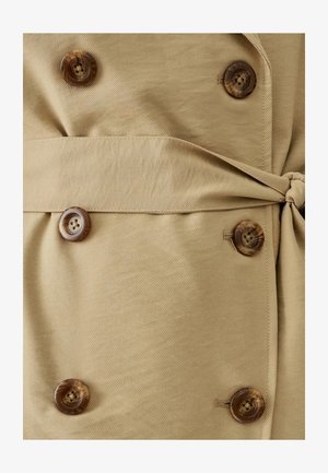 Manteau en tissu beige avec une surface texturée, doté de grands boutons marron, d'une ceinture à la taille et d'un design à double boutonnage.