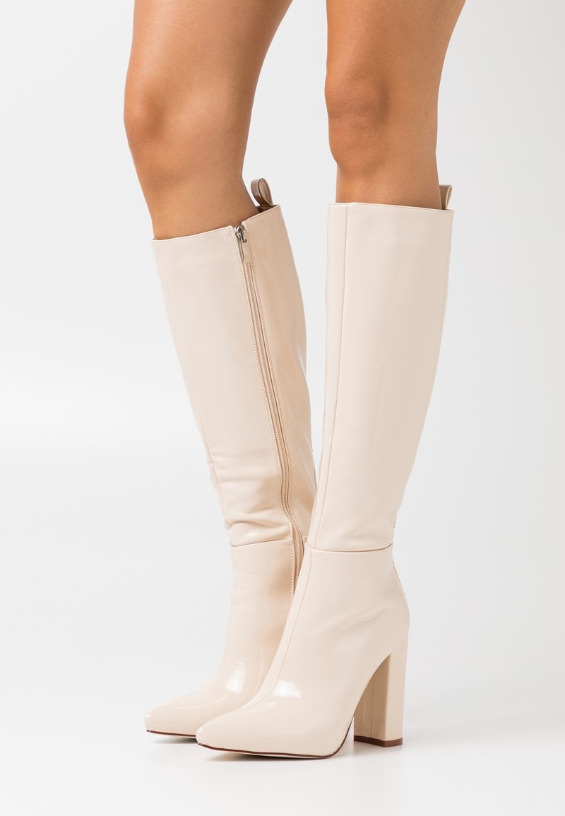 Botas de charol beige hasta la rodilla con punta cuadrada, tacón bloque y cremallera lateral. Textura suave y diseño minimalista.