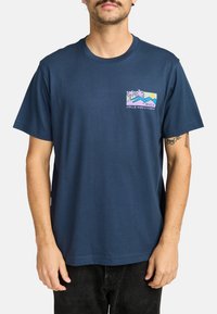 Marineblauwe t-shirt met korte mouwen, gemaakt van katoen, voorzien van een kleurrafiekk met palmbomen en bergen op de linkerborst.