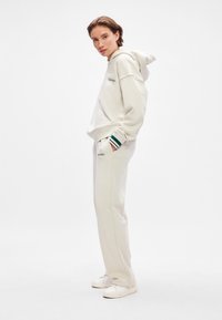 Light beige hoodie with a front pocket and "Calvin Klein" logo, paired with matching sweatpants featuring green-striped cuffs and brand logo.