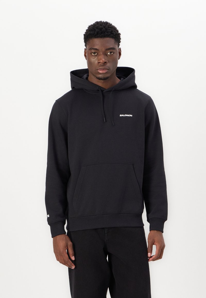 Haut à capuche noir en mélange de coton, doté d'une poche kangourou, d'une capuche avec cordon de serrage et d'un logo blanc sur la poitrine et la manche. Tissu texturé.