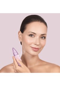 Appareil de nettoyage facial violet tenu dans une main, doté d'une pointe et d'une texture lisse, sur un arrière-plan rose doux.