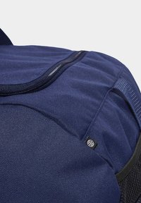 Námornícka modrá batoh s textúrovanou látkou, čiernym zipsom a malou logom značky. Má zosilnené popruhy a sieťované bočné vrecká.