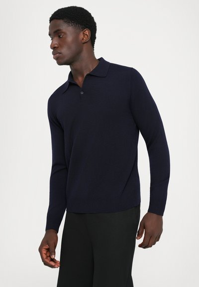 Navy långärmad polo skjorta med ribbad textur, krage och treknappsslutning. Har sidosprund och åtsittande manschetter för komfort.