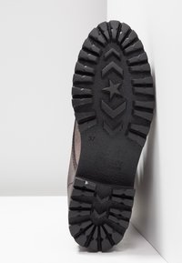 Semelle de botte en caoutchouc avec une surface noire texturée, présentant un motif de semelle géométrique et un détail en forme d'étoile central. Marquée "TOMMY JEANS" et taille 37.