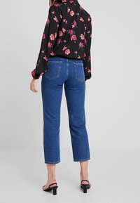 Svart blommig blus med rosa och gröna tryck, ihop med blå högmidjade jeans. Outfitten kompletteras med svarta klacksandaler.