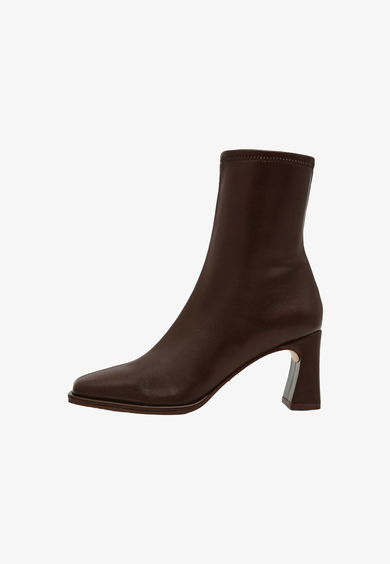 Stivale alla caviglia in pelle marrone con punta appuntita, parte superiore elasticizzata e tacco quadrato with accenti metallici. Textura liscia uniforme.