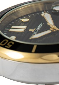 Reloj metálico en oro y plata con un dial texturizado negro, agujas blancas luminosas y un bisel negro con marcas de minutos.
