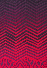 Textil mit einem Chevron-Muster in Rot- und Schwarztönen, mit komplexen floralen Details am Rand, hergestellt aus gewobenem Stoff.