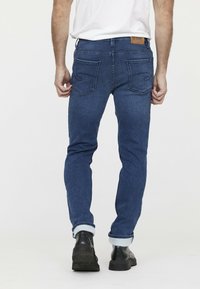 Donkerblauwe denim jeans met een slim fit, voorzien van een leren patch op de achterkant van de tailleband, en opgerolde pijpen over zwarte enkellaarzen.
