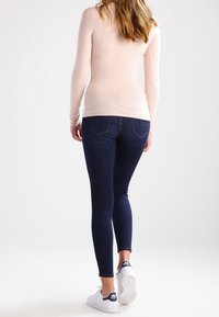 Långärmad ljusrosa topp i kombination med mörkblå skinny jeans och vita sneakers med marinblå detaljer, sedd bakifrån.