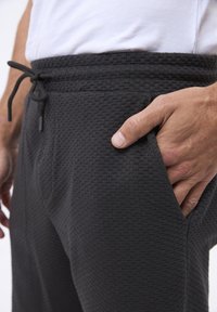 Karamelgrå sweatpants med et tekstureret stof, elastisk talje og justerbar snøre. Har sidelommer og en tapered pasform.