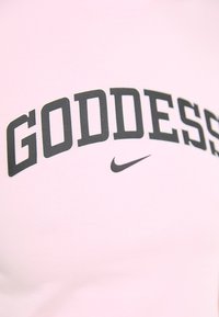 Pink t-shirt featuring the word "GODDESS" in bold black letters, with a small black Nike swoosh logo below the text.