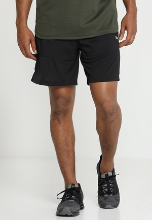 Pantalones cortos deportivos negros hechos de tela ligera, con una cintura elástica y dos bolsillos delanteros. Combinados con zapatillas negras para correr.