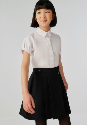Bela srajca s kratkimi rokavi in sprednjim zapenjanjem na gumbe, kombinirana z visoko pasno črno plisirano krilo z stranskim zadrgo in detajlom z gumbom.