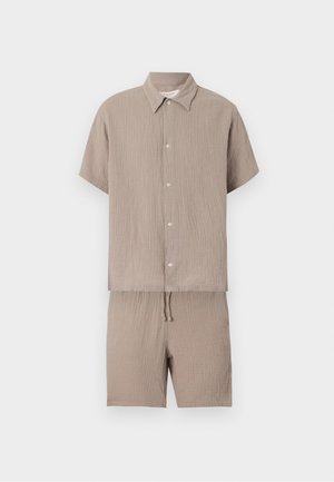 Beige overhemd met korte mouwen en knoopjes, gecombineerd met bijpassende short met trekkoord, beide gemaakt van een lichtgewicht, getextureerde stof.