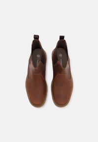 Chaussures slip-on en cuir marron avec des panneaux élastiques sur les côtés, design courbé et détails de couture beige le long de la semelle.