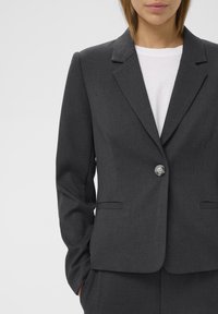 Sötétszürke blézer, amelynek hajtókás gallérja, egygombos záródása és két elülső zsebe van, sima, texturált anyagból készült.