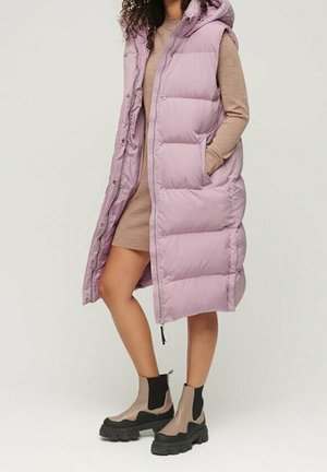 Lång, puffy lavendelfärgad väst med huva, utrustad med dragkedja och tryckknappar, i kombination med knähöga, tan- och svartfärgade chelsea-boots.