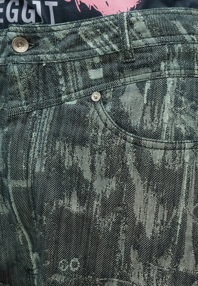 Σκούρα πράσινα τζιν από denim με υφή μοτίβου και ελαφρύτερες αποχρώσεις, καθώς και ασημένιο μεταλλικό εξάρτημα για τα κουμπιά.