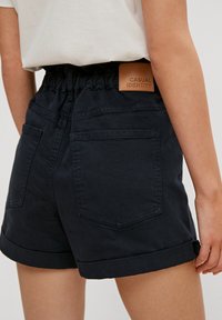Shorts en jean bleu marine avec une taille élastique froncée, des ourlets retroussés, deux poches arrière et une étiquette de marque en cuir marron à l'arrière.