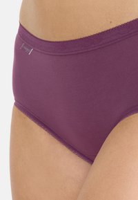 Ciemnofioletowe bawełniane majtki z miękkim pasem, z delikatnym falbanym wykończeniem oraz małą metką marki z boku.