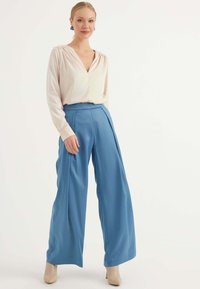 Blus i ljusrosa med V-ringning och långa ärmar, ihop med vida, högmidjade blå byxor. Beiga klackar fulländar outfiten.