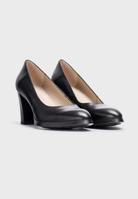 Zapatos de tacón alto de piel negra con punta redondeada y un tacón de bloque de madera texturizada. Superficie lisa con detalles mínimos y sin hardware visible.