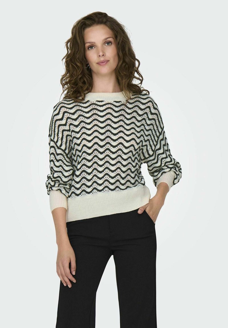 Maglione lavorato a maglia nero e crema con motivo a onde, scollatura a barca e polsini a costine; abbinato a pantaloni neri. Vestibilità comoda e tessuto testurizzato.