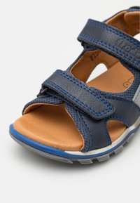 Blå lær sandaler med to justerbare borrelås, beige innersåle, åpen tå-design og grå gummisåle med blå detaljer.