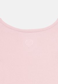 Tissu rose clair avec un petit motif de cœur cousu au centre supérieur sous un col arrondi.