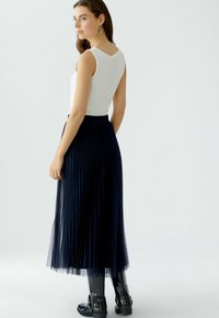 Un débardeur blanc côtelé associé à une jupe en tulle plissée navy. La tenue est complétée par des bottes noires à genoux avec des boucles et une légère brillance.