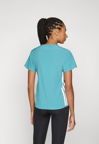 Aquamarine træningsskjorte med korte ærmer, der har perforeret tekstur og hvide sidelister, kombineret med sorte leggings.