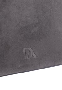 Material de ante negro con una textura suave, que presenta un detalle de logo en relieve. El diseño es minimalista y moderno.