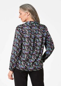 Blusa nera con un motivo astratto colorato in verde, viola e bianco. Maniche lunghe, chiusura con bottoni sul retro, tessuto morbido e vestibilità comoda.