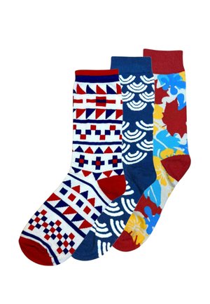 Trzy kolorowe skarpetki o różnych wzorach: czerwona, biała i niebieska z geometrycznym wzorem; granatowa z białymi półokręgami; oraz wielokolorowa w kwiaty z czerwonymi akcentami.