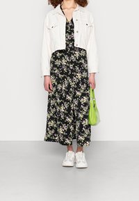 Svart blommig klänning med V-ringning, en vit kort denimjacka, vita sneakers och en grön väska. Klänningen har små lila och rosa blommor.