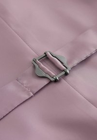 Detailný záber na fialovoružový textilný remienok prevlečený striebornou obdĺžnikovou prackou s zaoblenými hranami na hladkom materiáli.