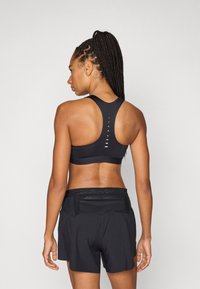 Μαύρο αθλητικό σουτιέν με σχεδιασμό racerback και οριζόντια ανοίγματα στην πλάτη, συνδυασμένο με άνετα μαύρα σορτς με λογότυπο στη μέση.