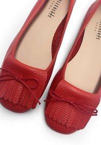 Bailarinas de cuero rojo con un acabado texturizado, detalle de flecos en la punta y un acento de lazo. Forro interior suave y forma redondeada.