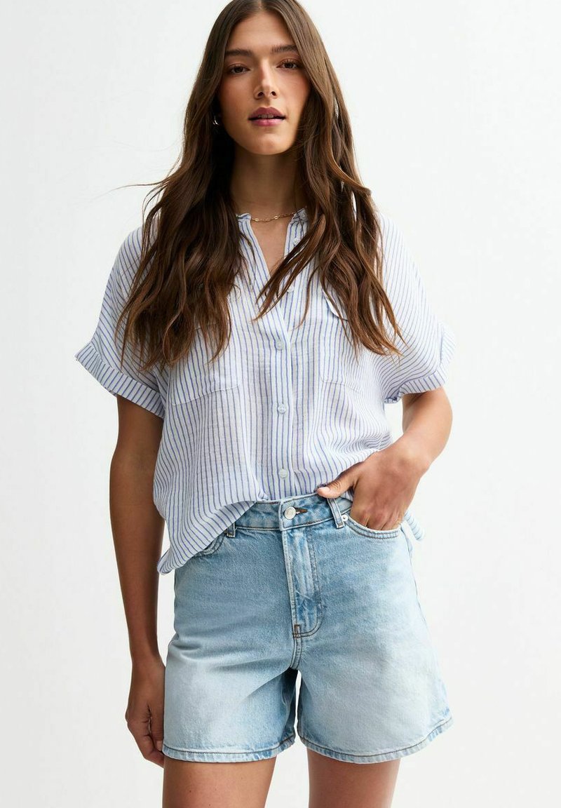 Chemise à rayures bleu et blanche à boutons, à manches courtes et coupe décontractée, associée à un short en denim délavé à taille haute.