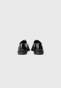 Chaussures en cuir noir avec une finition lisse, des bouts ronds, des petits talons et des coutures décoratives sur les côtés. Convient pour les occasions formelles.