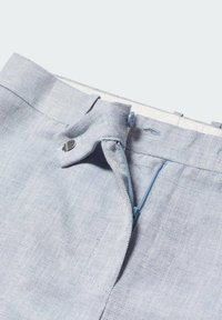 Pantalon en tissu chevron bleu clair avec fermeture éclair, bouton et agrafe latérale à la taille, montré partiellement ouvert.