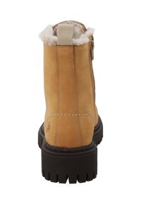 Tan suède winterboot met dikke zwarte lugzool, zichtbare zijsluiting, lus trekkabel en witte pluizige voering aan de bovenrand.